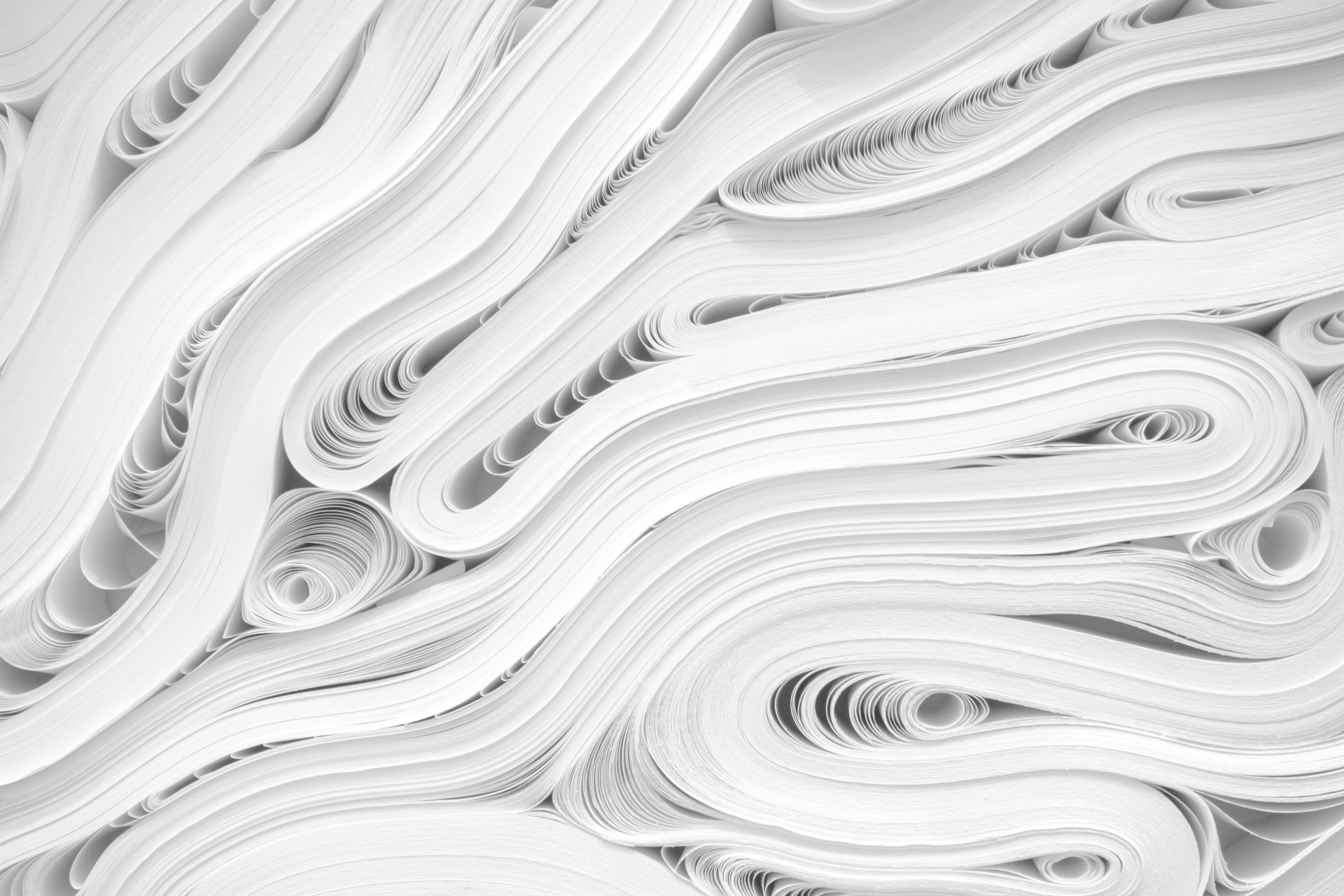Close-up of stacked white paper sheets curled into flowing, wavy layers.